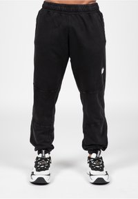 Zwarte joggingsbroek met een elastische tailleband, taps toelopende boorden en contrasterende stiksels. Bevat een klein logo op de linkerdij.