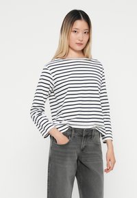 Camicia a maniche lunghe bianca con strisce blu navy, realizzata in un tessuto morbido. Abbinata a jeans grigi, con una vestibilità comoda e tasche frontali.