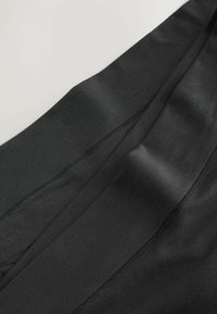 Gros plan sur un tissu noir avec des coutures visibles et une texture lisse, montrant des coutures détaillées sur une surface de vêtement douce.