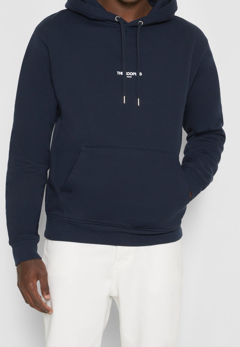 Námořnická modrá bavlněná mikina s kapucí, stahovací šňůrkou a klokankou. Na hrudi se nachází bílý nápis "THE KOOPLES PARIS" a žebrované manžety.