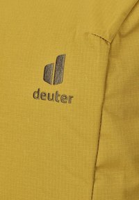 Gele stof met een zwart gestikt "deuter" logo dat uit twee verticale vormen bestaat en de merknaam eronder.