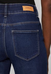 Dunkelblaue Denim-Jeans mit einem Lederetikett mit der Aufschrift "ONLY" am Bund, ausgestattet mit einem klassischen Fünf-Taschen-Design und kontrastierenden Nähten.