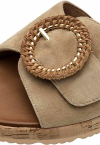 Sandale en suède beige avec un accent circulaire tissé, une semelle intérieure marron et une semelle en liège avec une surface texturée.
