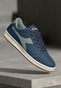 Navy-blue sneakers with light gray accents, smooth synthetic and suede-like texture, round toe, white sole, and stitched detailing on the upper.