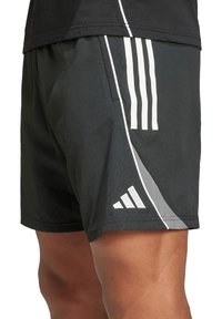 Pantaloncini sportivi neri realizzati in tessuto leggero. Presentano tre strisce verticali bianche e un accento grigio sul lato. Include una tasca.