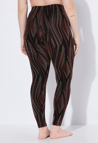 Leggings neri con un motivo a zigzag in rosso e oro, realizzati in tessuto elasticizzato e con un'alta vita, progettati per comodità e flessibilità.