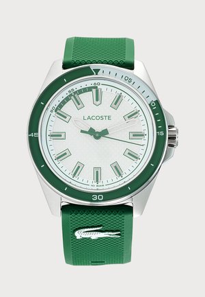 Zelené a strieborné hodinky Lacoste s bielym ciferníkom, zelenými hodinovými značkami a zeleným textúrovaným remienkom s bielym logom krokodíla.