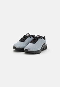 Zapatillas deportivas de malla gris con acentos negros, que presentan una superficie texturizada, puntera redondeada y un talón acolchado con unidades de aire visibles.