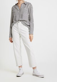 Camicia a righe grigia e bianca con bottoni, due tasche frontali, abbinata a pantaloni denim bianchi corti e sneakers bianche alte.