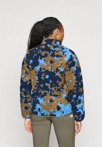 Fleecejack met een blauw, bruin en marineblauw spetterpatroon. Hoge nek, lange mouwen en een relaxte pasvorm.