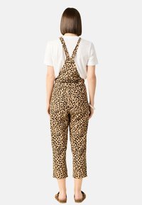 Luipaardprint overal met verstelbare bandjes, verkorte benen en een aansluitende achterkant, gecombineerd met een eenvoudig wit T-shirt en beige sandalen.