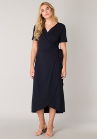 Marineblaues Wickelkleid mit kurzen Ärmeln, weichem Stoff, V-Ausschnitt und seitlichem Bindeband. Hat einen fließenden Saum, der bis zur Mitte der Wade reicht.