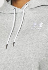 Sweat à capuche gris Under Armour avec cordons blancs et embouts métalliques argentés, montrant un col partiel et un logo sur la poitrine.