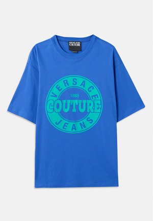 Kék pamut póló rövid ujjakkal, a közepén zöld színű kör alakú logóval, amelyen a "VERSACE COUTURE JEANS 1988" felirat olvasható.