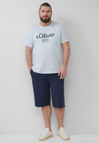 T-shirt en coton bleu clair avec texte noir, associé à un short navy. Le modèle porte des baskets blanches. Tenue simple et décontractée avec une coupe relaxée.