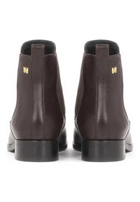 Botas de tobillo de cuero marrón con una textura suave, paneles laterales elásticos y un tacón bajo en bloque. Cuenta con un acento de logo dorado en el tacón.