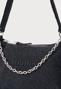 Fekete farmer anyagból készült kézitáska ezüst láncpánttal és dombornyomott "tommy jeans" logóval. Cipzáras záródással és puha tapintással rendelkezik.