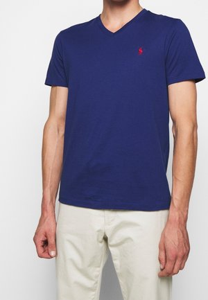 Granatowy bawełniany t-shirt z dekoltem w serek i krótkimi rękawami, z małym czerwonym haftowanym logo na lewej piersi. Gładka faktura, dopasowany krój.