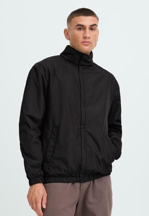 Schwarze Nylonjacke mit hohem Kragen, Reißverschluss und elastischen Bündchen. Verfügt über Seitentaschen und eine leichte, glatte Textur.