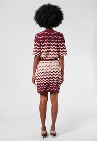 Neulemekko, jossa on aaltoileva kuvio burgundinpunaisena ja vaaleanpunaisena, lyhyillä hihoilla ja tiukalla vyötäröllä. Sileä kangas ja polvipituus.