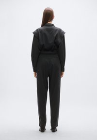 Črni kombinezon s poudarjenim pasom, prevelikim ramenskim dizajnom in dolgimi rokavi. Gladek tekstura, z vgrajenimi žepi in krojenim pristajanjem.