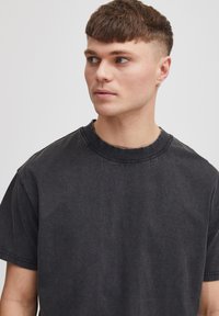 Tricou negru din bumbac, cu mâneci scurte, de tip crew neckline și o croială relaxată. Materialul are o textură subtilă și un aspect decolorat.