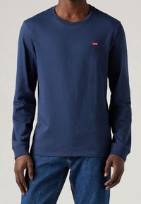 Granatowa koszulka z długim rękawem, wykonana z bawełny, z okrągłym dekoltem i małym czerwonym logo Levi's na piersi. Gładka tekstura.