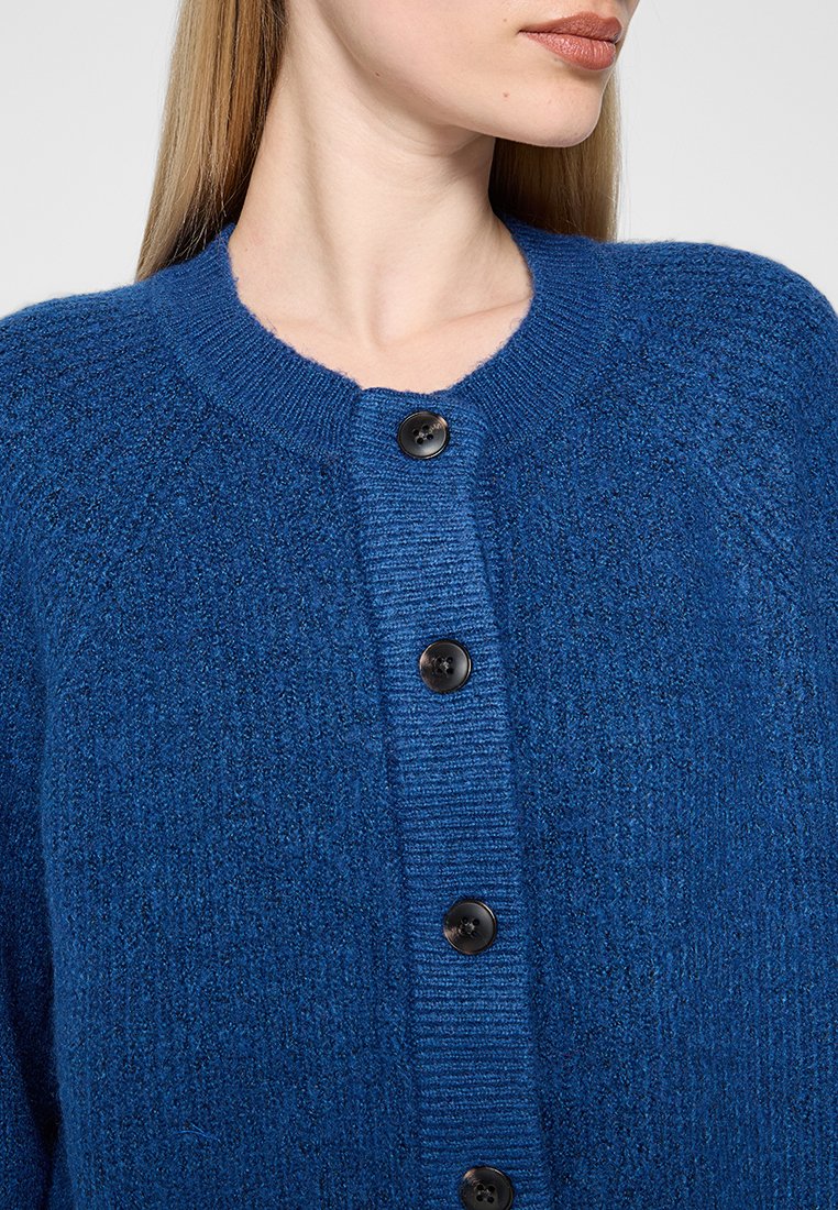 Blauer Strickcardigan mit Rundhalsausschnitt, ausgestattet mit sechs schwarzen Knöpfen und einem strukturierten Stoff. Das Design beinhaltet gerippte Akzente entlang der Knopfleiste.