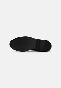 Suela de zapato negra con un acabado liso, forma ligeramente curvada y un patrón de agarre texturizado. Tacón reforzado para mayor durabilidad.