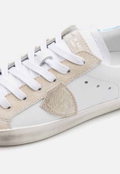 Hvite lær-sneakers med beige semsket skinn-detaljer, teksturert logo-patch og hvite lisser. Har perforert design på siden og slitt yttersåle.