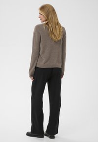 Pull en maille douce marron avec une coupe décontractée, associé à un pantalon large noir et des bottes noires. La texture est lisse avec des poignets côtelés.