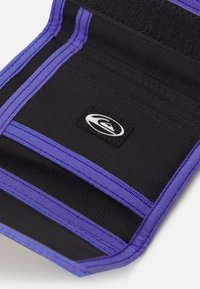 Black fabric product with purple stitching and detailing, featuring a textured surface and a small logo patch in the corner.