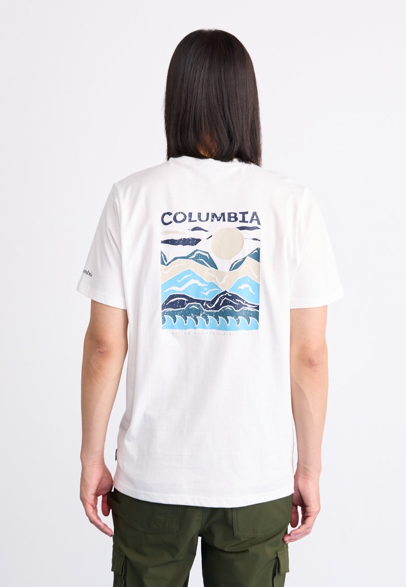 Biała bawełniana koszulka z krótkim rękawem, z niebiesko-beżowym wzorem przedstawiającym góry i fale, z napisem "COLUMBIA" powyżej.