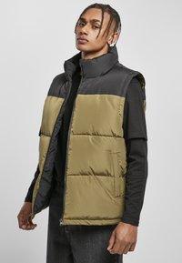 Polstret vest med en sort topsektion og en olivengrøn bund, med lynlåslukning, høj krave og sidelommer, lavet af syntetisk materiale.