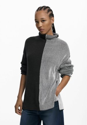 Strickpullover mit einem Stehkragen, einer schwarzen Seite und einer vertikal gestreiften weißen Seite. Lockerer Schnitt mit hochgerollten Ärmeln und seitlichen Schlitzen.