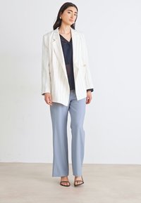 Blazer blanco con rayas finas sobre una blusa negra, combinado con pantalones azul claro y sandalias negras. Tejido suave con un corte ajustado y diseño estructurado.