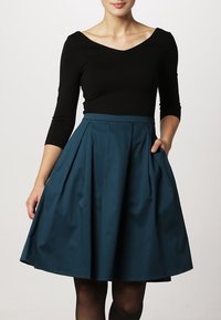 Top negro ajustado con un escote en V profundo, combinado con una falda plisada en color teal hasta la rodilla que cuenta con bolsillos laterales y una textura suave.