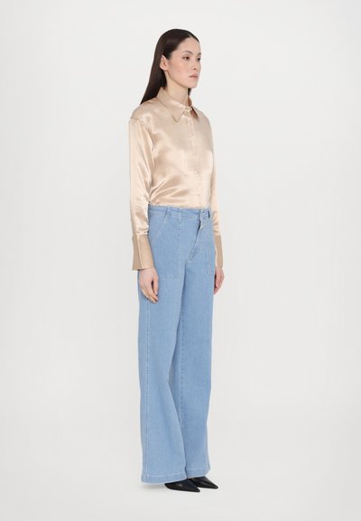 Beige satin long-sleeve shirt with a collar, paired with light blue wide-leg denim jeans. Black pointed-toe shoes complete the outfit.