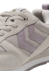 Jasno beżowe sneakersy z połączeniem teksturowanej zamszowej skóry i siateczki. Wyraźne lawendowe akcenty w kształcie chevronu oraz tonowane sznurowadła na gumowej podeszwie.