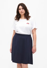 T-shirt blanc à manches courtes avec une broderie de cerise rouge sur la poitrine, associé à une jupe bleu marine à mi-genoux avec une taille élastique.