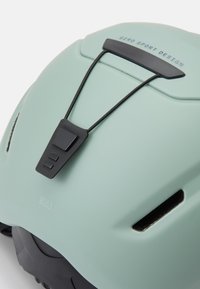 Miętowo zielony kask o matowym wykończeniu, z czarnym systemem regulacji, otworami wentylacyjnymi oraz logiem "GIRO SPORT DESIGN" na górze.