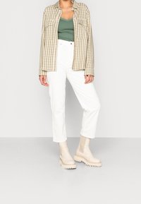 Camicia a quadre beige, canotta verde, pantaloni bianchi e stivali chunky color crema. Texture principali: tessuto a quadri e materiale degli stivali liscio.