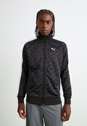 Black jacket with repeating logo pattern, high collar, zippered front, and white side stripes. Ribbed cuffs and hem, smooth fabric texture.