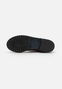 Black rubber sole with textured tread pattern, featuring a smooth brown upper. Reinforced heel and minimal branding visible.