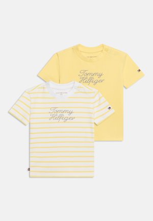 Deux t-shirts à manches courtes pour tout-petits, un jaune uni et un blanc avec des rayures jaunes, tous deux avec le texte "Tommy Hilfiger" à l'avant.