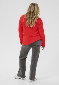 T-shirt rouge à manches longues associé à un pantalon large gris et des baskets blanches, présentant une coupe décontractée et un design basique, vu de dos.