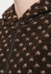 Brązowa bluza z polaru na zamek, wykonana z teksturowanej tkaniny z kremowymi wzorami przypominającymi gwiazdki oraz przednim zamkiem błyskawicznym.