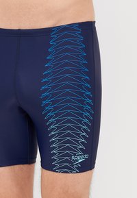 Σαπούνια κολύμβησης Speedo σε ναυτικό μπλε με μπλε ζιγκ-ζαγκ σχέδιο στο πλάι; κατασκευασμένα από ελαστικό υλικό, προσφέροντας άνετη εφαρμογή και επίπεδες ραφές.