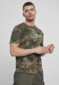 Žalias kamufliažo rašto T-shirt iš minkštos medžiagos, su trumpomis rankovėmis ir apvaliu kaklu, derinamas su alyvuogių spalvos šortais.