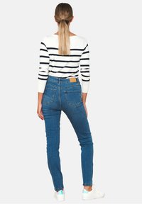 Blue high-waisted jeans with a slim fit and back pockets, paired with a striped black and white sweater. White sneakers complete the look.